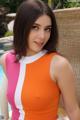 A woman in an orange and pink dress sitting by a pool.