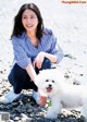 A woman kneeling down next to a white dog on a beach.