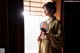 A woman in a kimono holding a fan in front of a window.