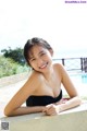 A woman in a black bathing suit leaning against a wall.